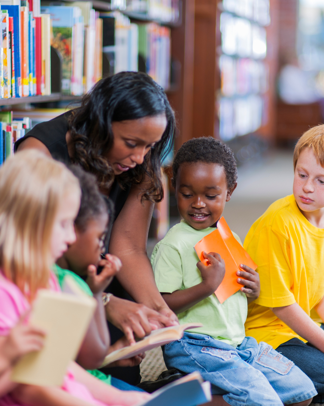 A teacher reads aloud to a diverse group of children holding books in a library.