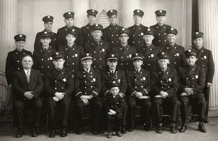 A vintage black-and-white portrait of a large group of fire department personnel in uniform, with one child in the center.