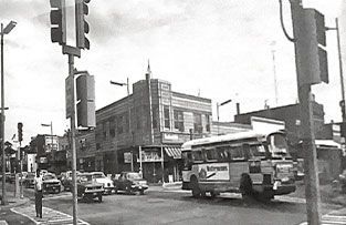 A black-and-white street scene shows a bus turning at a city intersection with surrounding buildings and traffic signals.