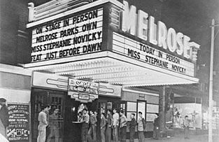 A line of people stands outside the Melrose Theater under a marquee promoting an in-person appearance by Stephanie Novicky.