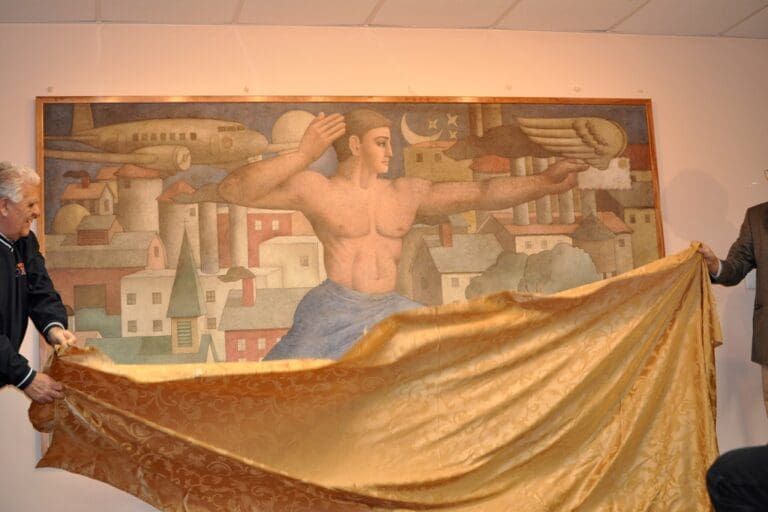 Two people unveil a framed mural depicting a muscular figure over a townscape with an airplane and winged envelope.