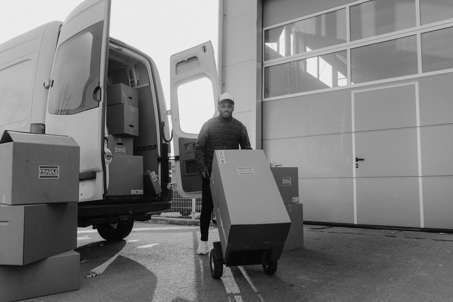 Person unloading boxes from a van using a dolly. Warehouse exterior.
