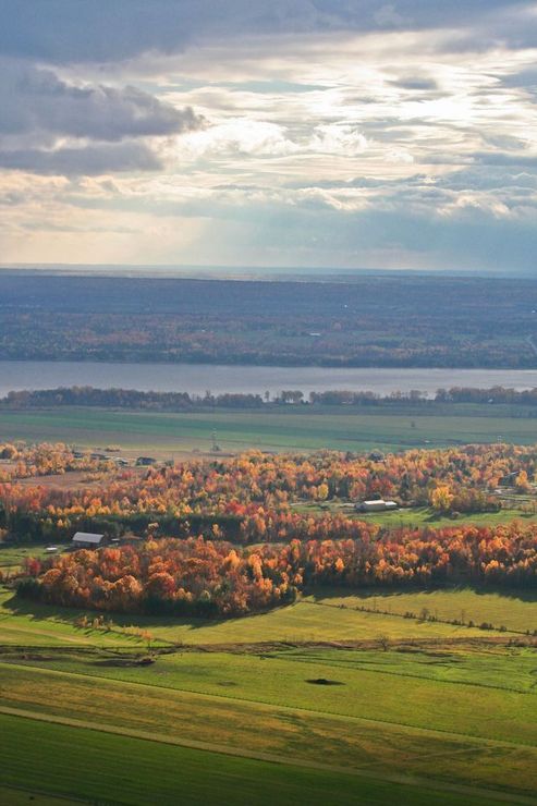 Overlooking a landscape of fields, autumn trees, and a lake under a cloudy sky.