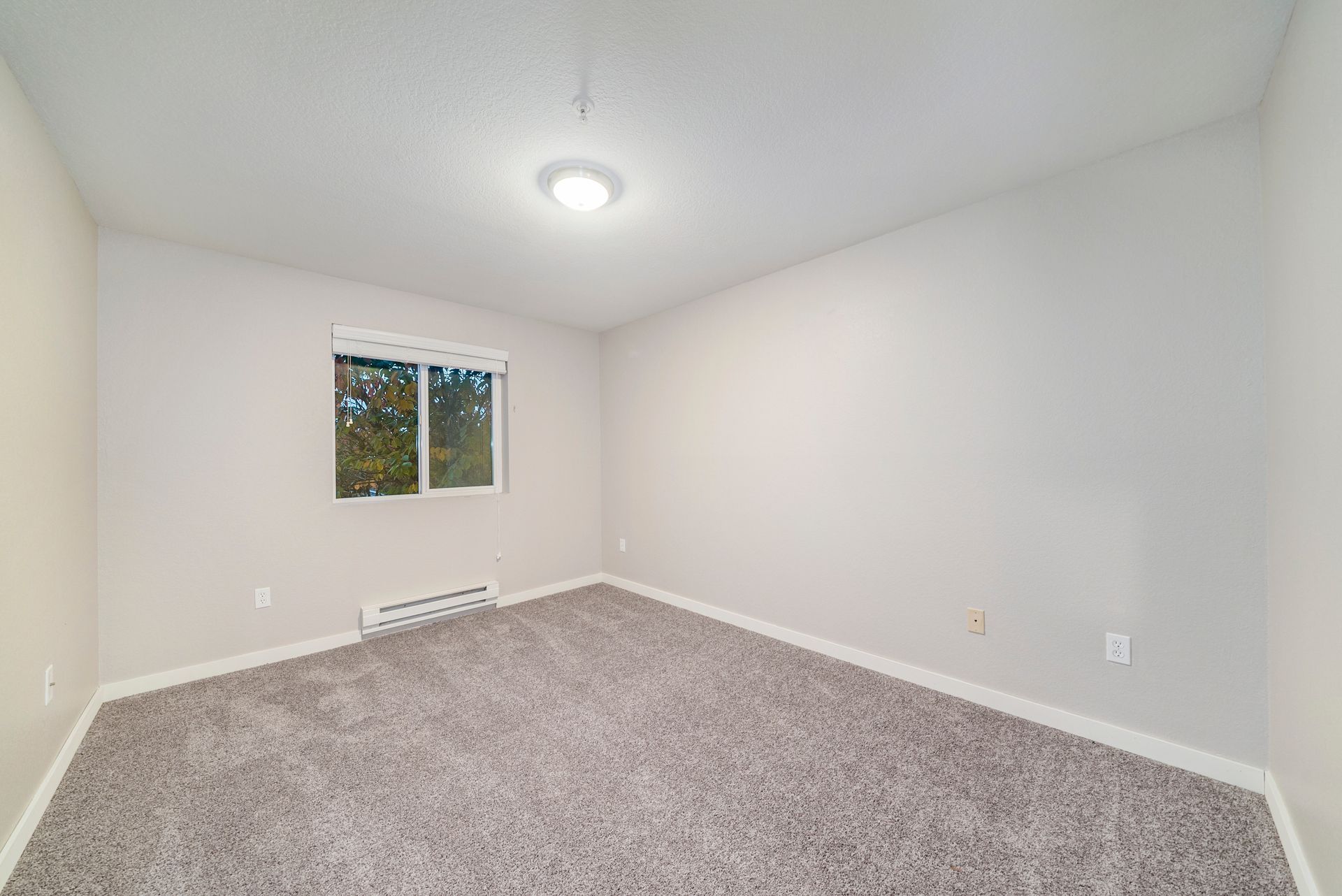 An empty bedroom with a carpeted floor and a window.