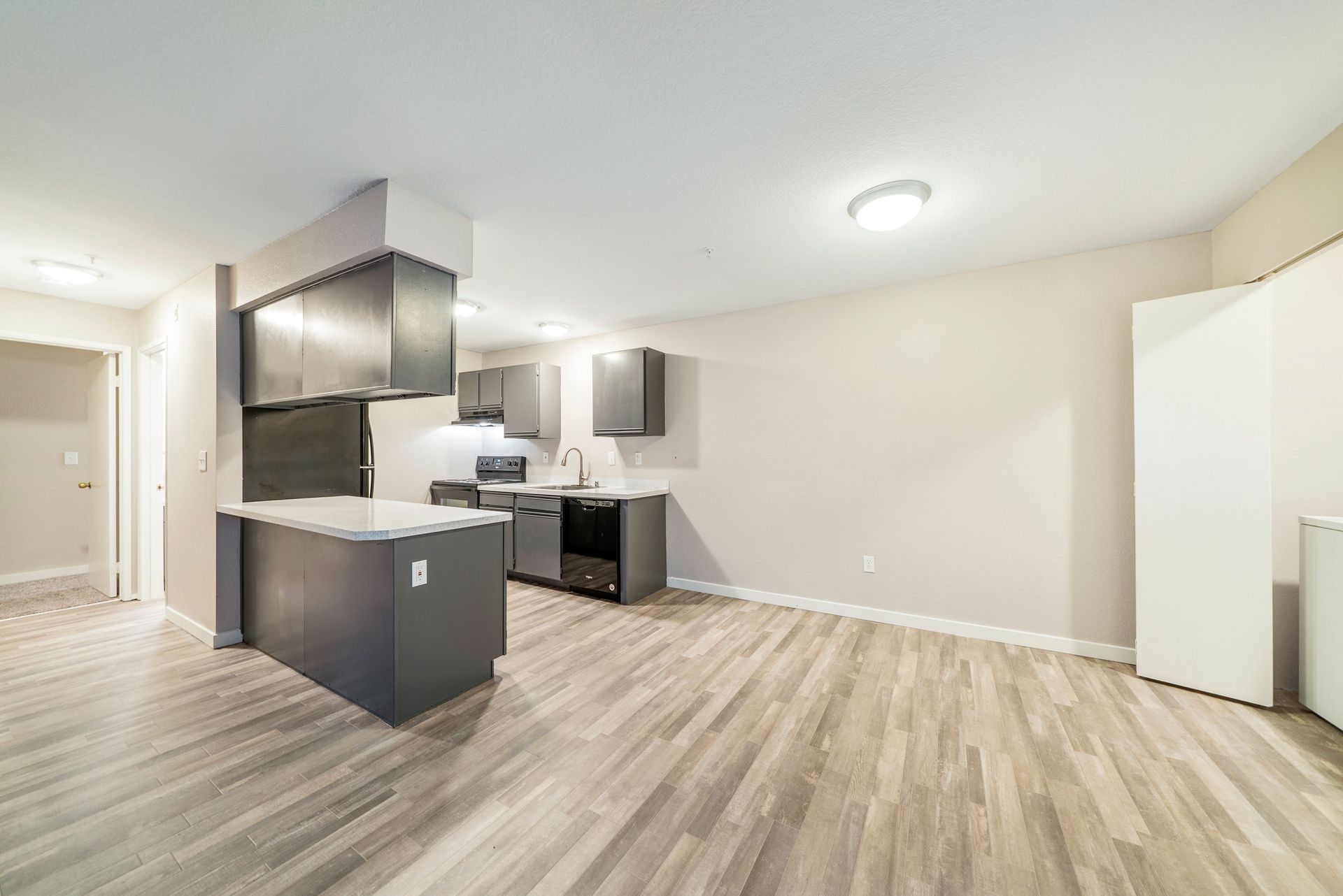 An empty apartment with hardwood floors and a kitchen.