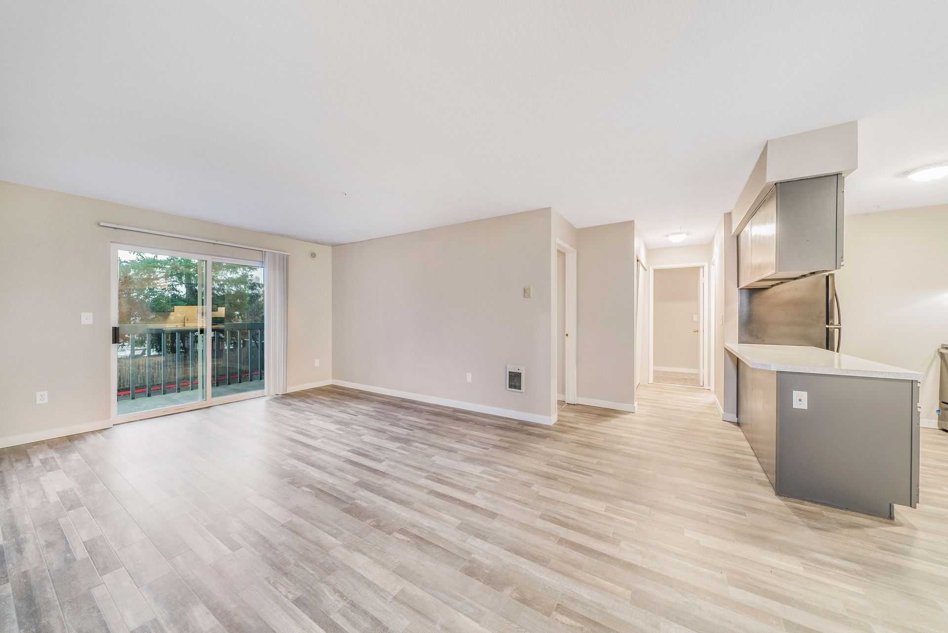 An empty living room with hardwood floors and sliding glass doors leading to a balcony.
