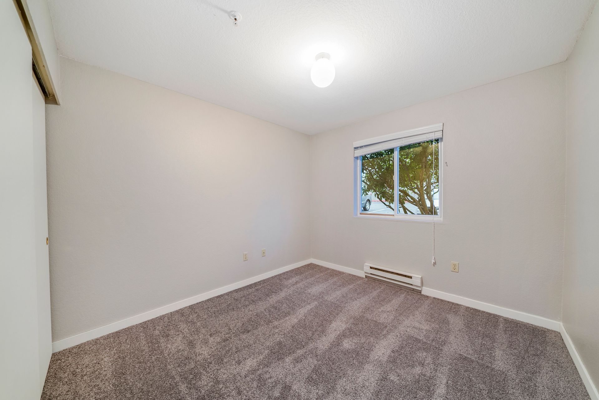 An empty bedroom with a carpeted floor and a window.