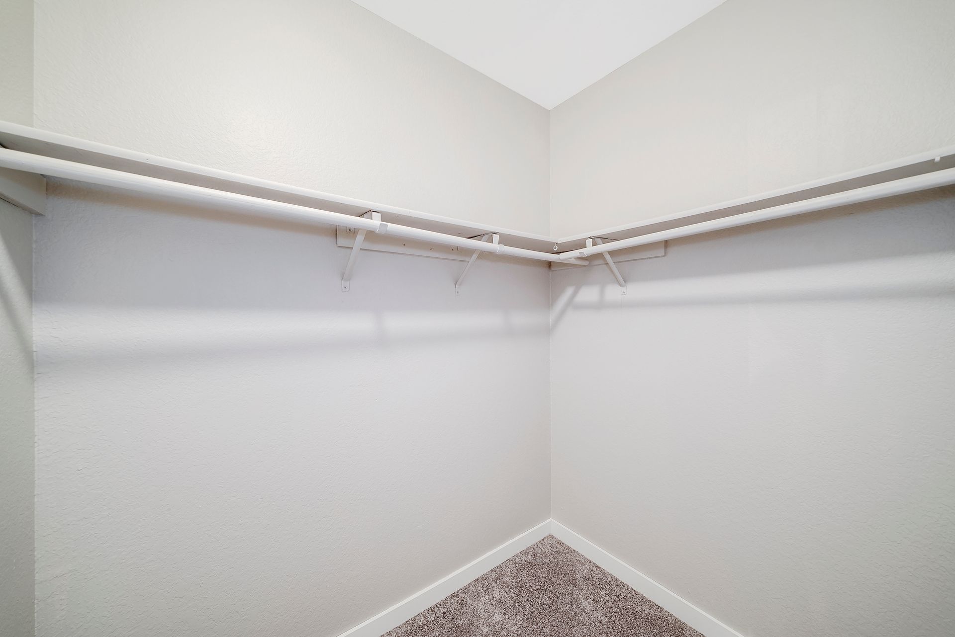 An empty walk in closet with a carpeted floor and white walls.