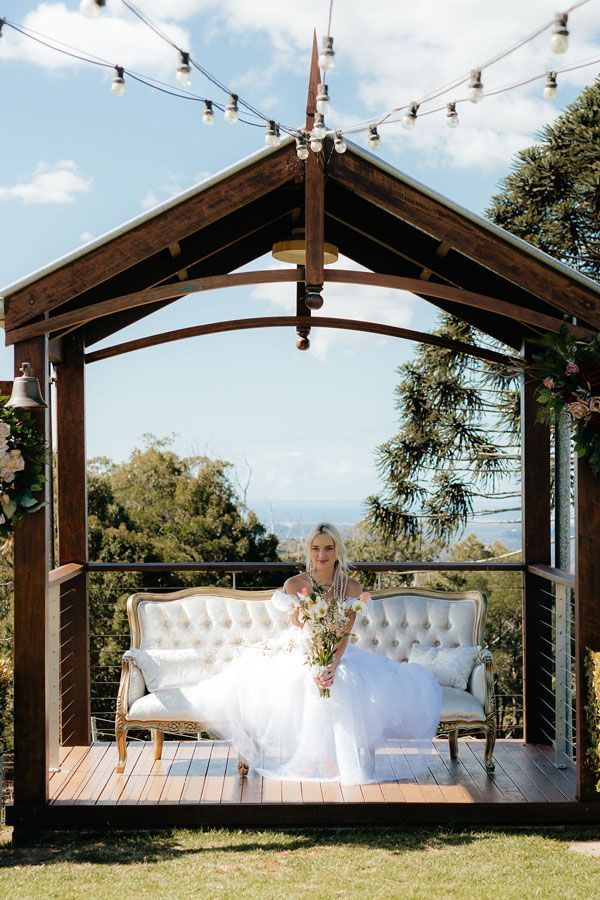 A Bride in a Wedding Dress is Sitting on a Couch Under a Gazebo — Prim n Proper Event Hire in Palmview, QLD