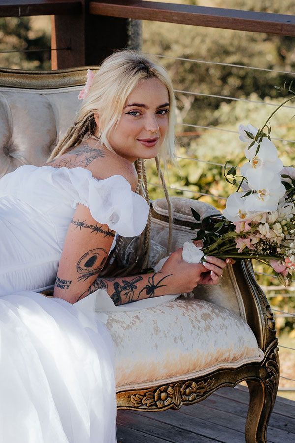 A Woman in a White Dress is Sitting on a Chair Holding a Bouquet of Flowers — Prim n Proper Event Hire in Palmview, QLD
