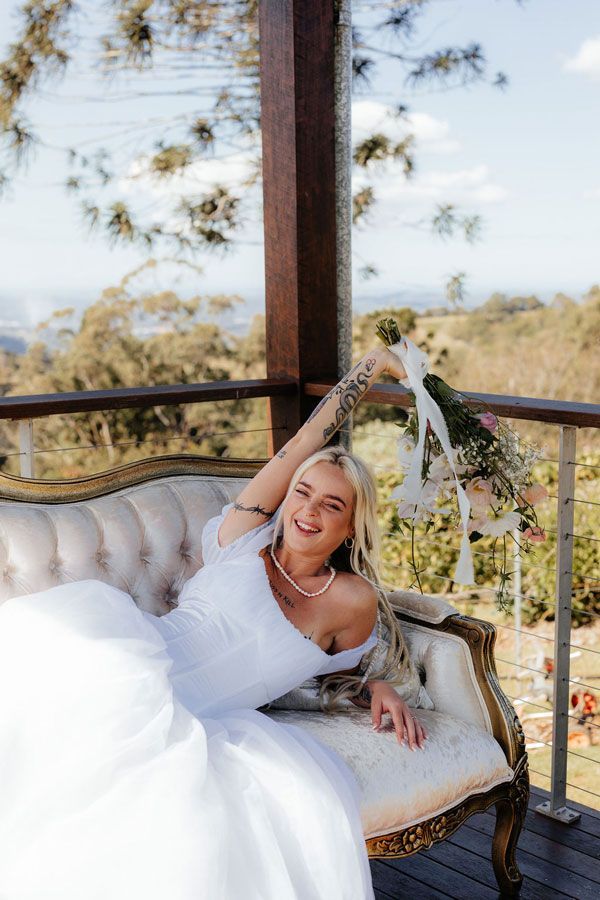 A Woman in a Wedding Dress is Sitting on a Couch on a Balcony — Prim n Proper Event Hire in Palmview, QLD