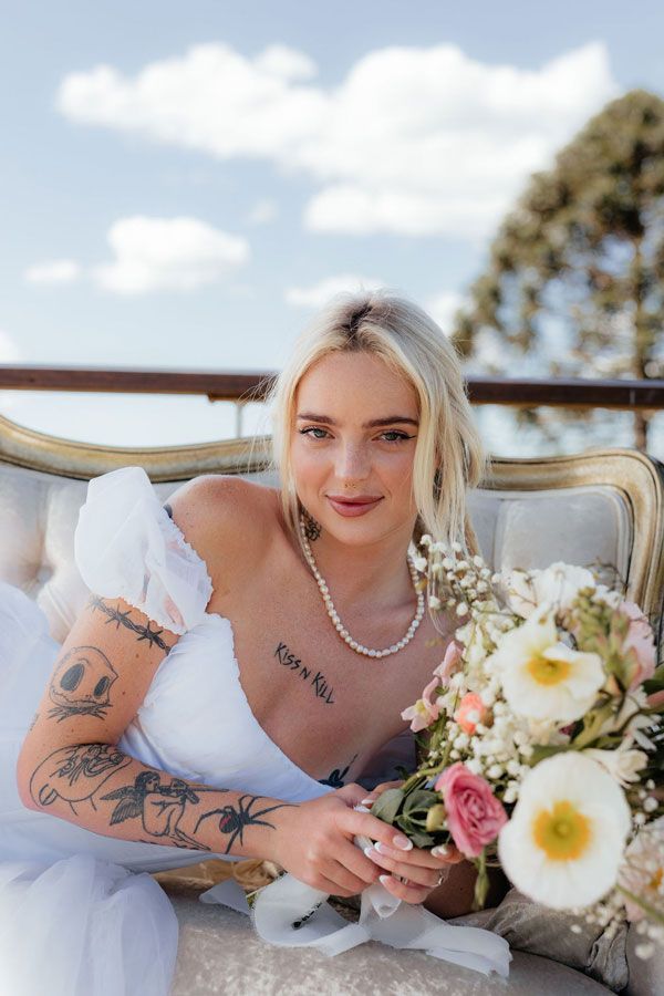 A Woman in a White Dress is Sitting on a Couch Holding a Bouquet of Flowers — Prim n Proper Event Hire in Palmview, QLD