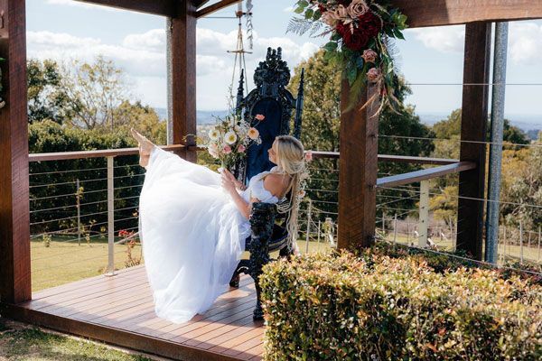 A Bride in a White Dress is Sitting on a Chair Under a Gazebo — Prim n Proper Event Hire in Palmview, QLD