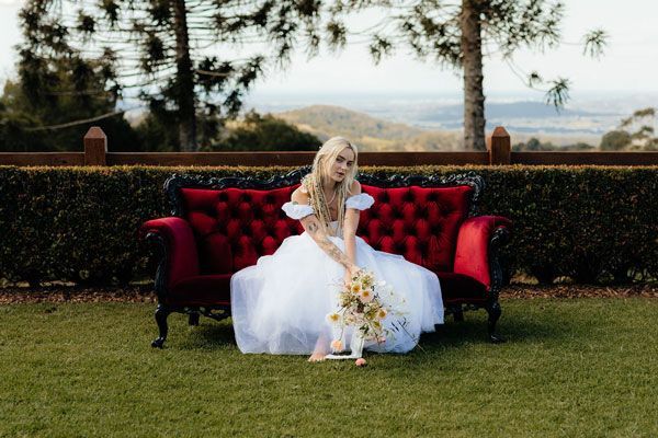 A Bride in a White Dress is Sitting on a Red Couch — Prim n Proper Event Hire in Palmview, QLD