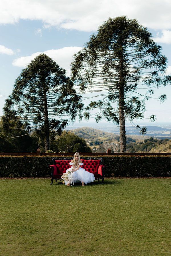 A Woman in a White Dress is Sitting on a Red Couch in a Field — Prim n Proper Event Hire in Palmview, QLD