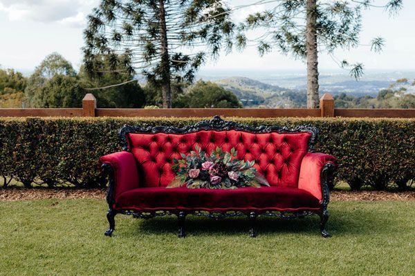 A Red Couch With Flowers on It is Sitting on Top of a Lush Green Field — Prim n Proper Event Hire in Palmview, QLD