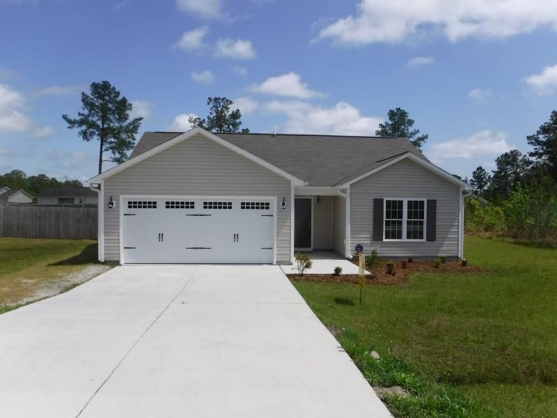 Gray single-story house with a white garage door and concrete driveway on a sunny day.
