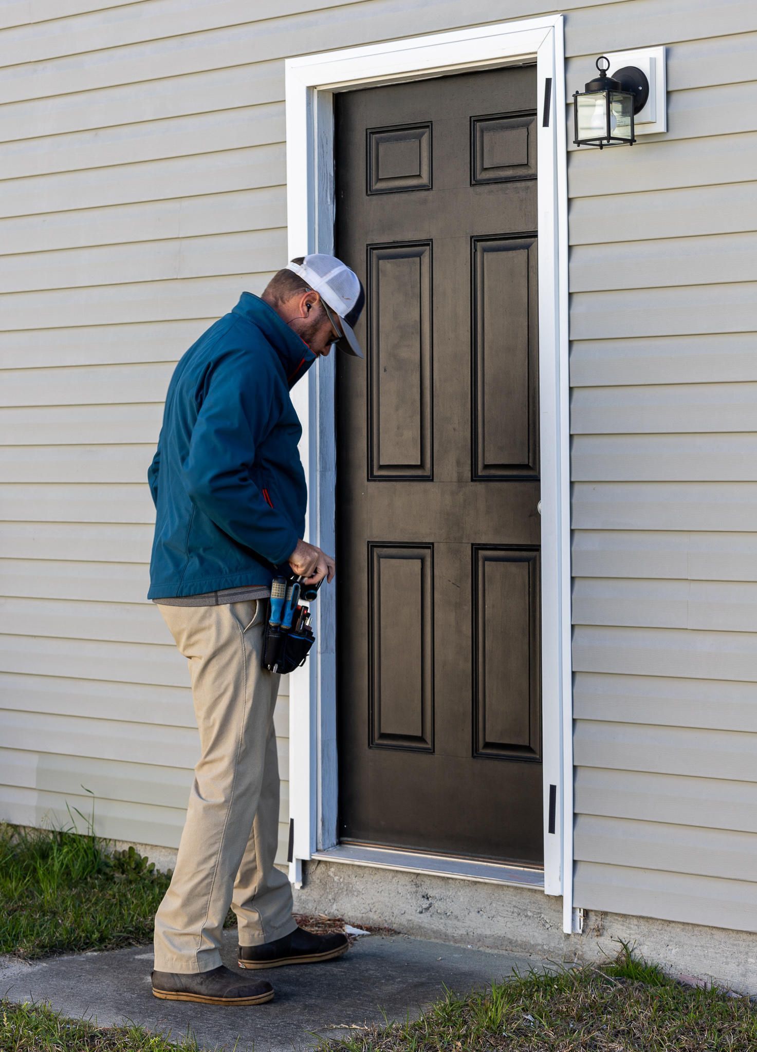 Man in blue jacket inspects a brown door with white trim outside a building.