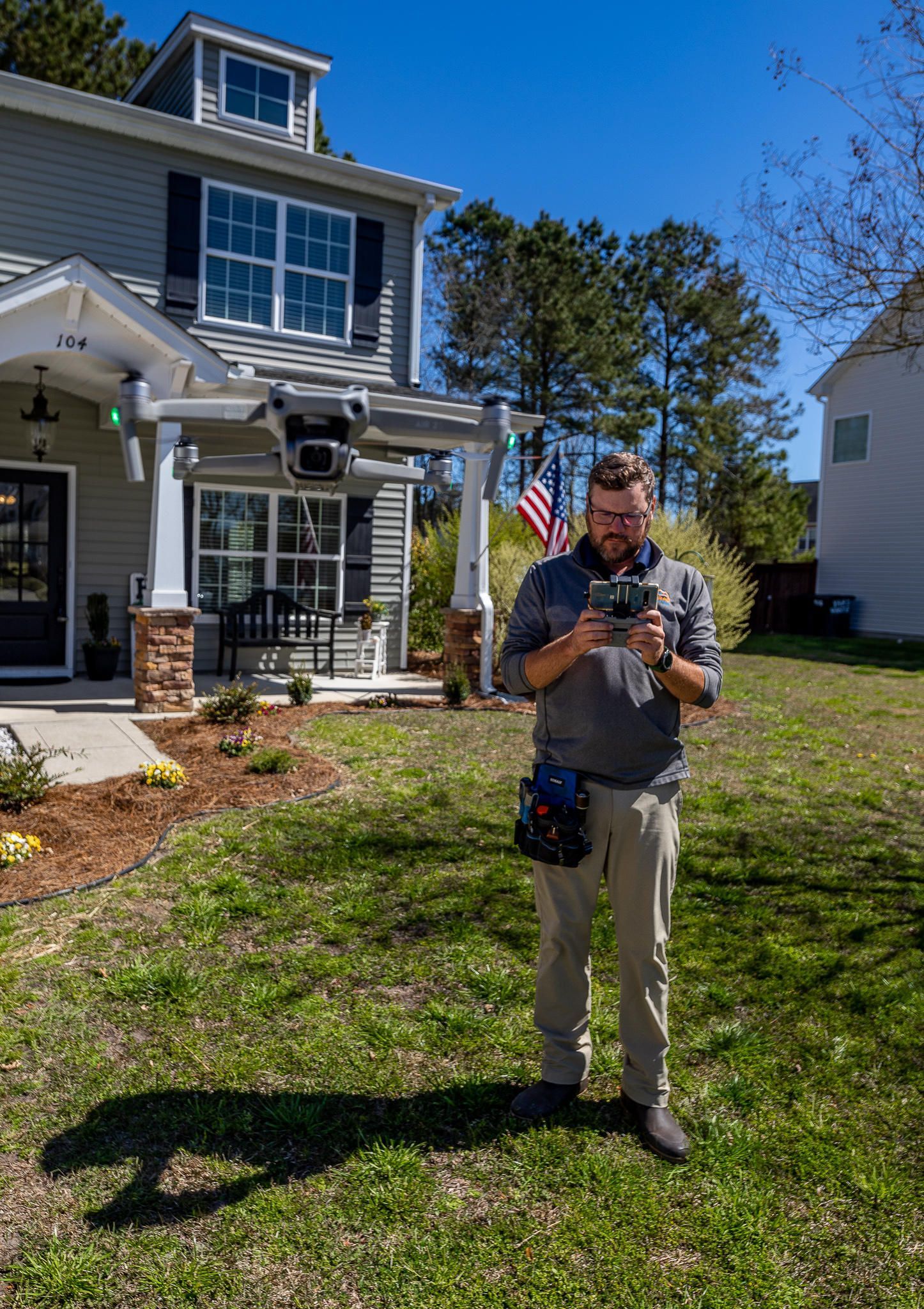 Man operating drone in front of a house on a sunny day.