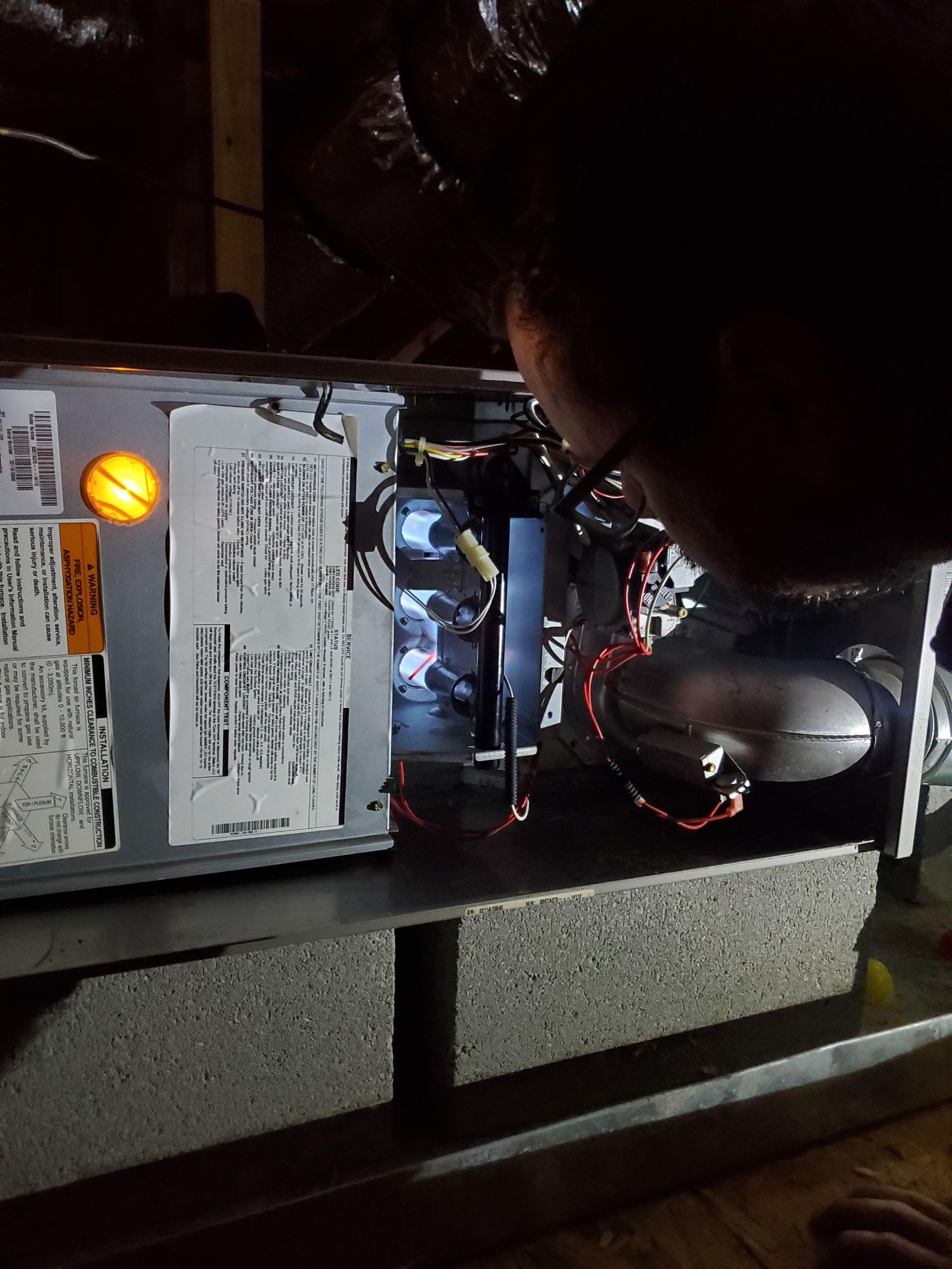 Person working on the open interior of an HVAC unit, illuminated by a light.