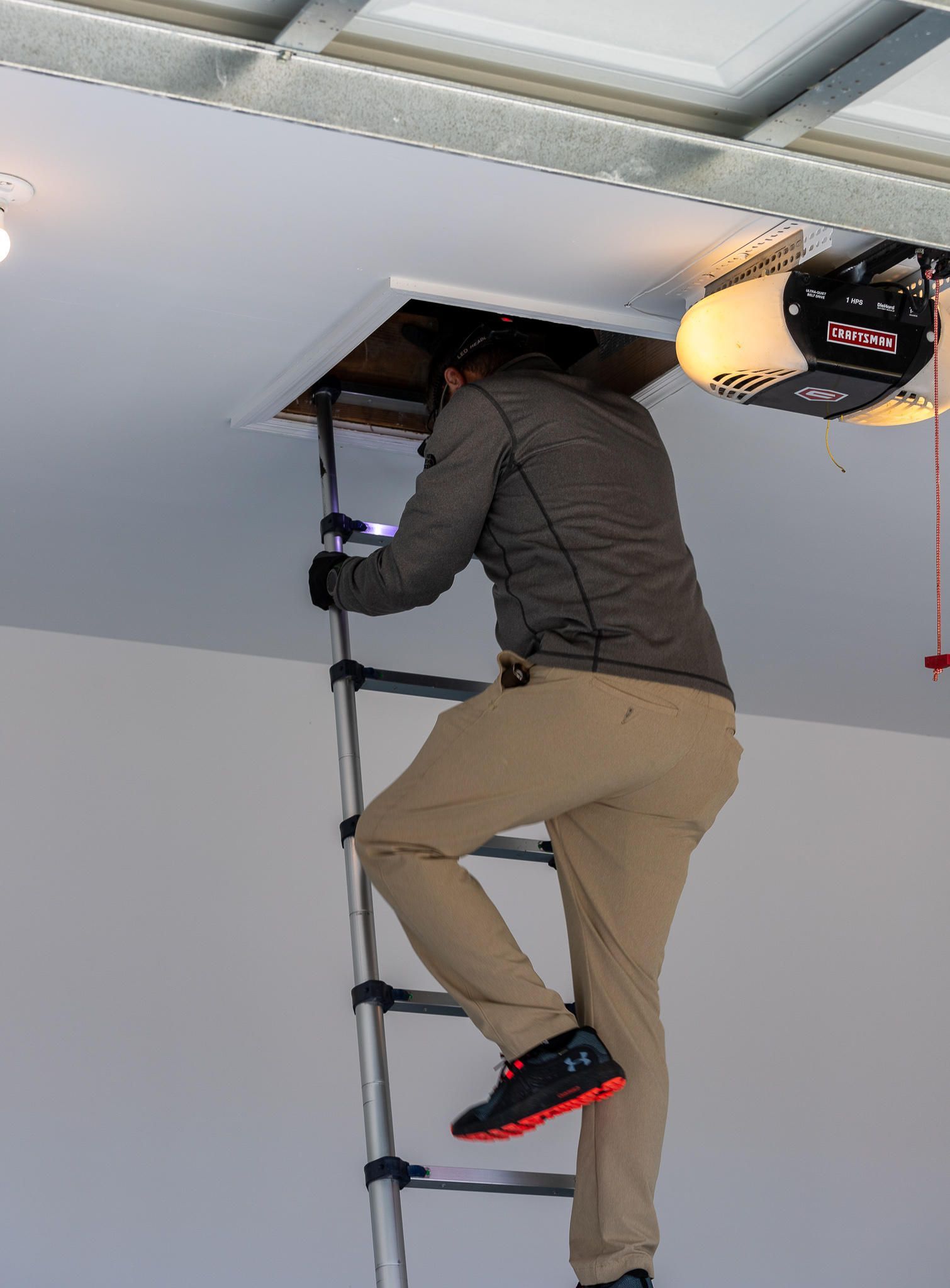 Person on ladder entering a ceiling access panel in a garage.