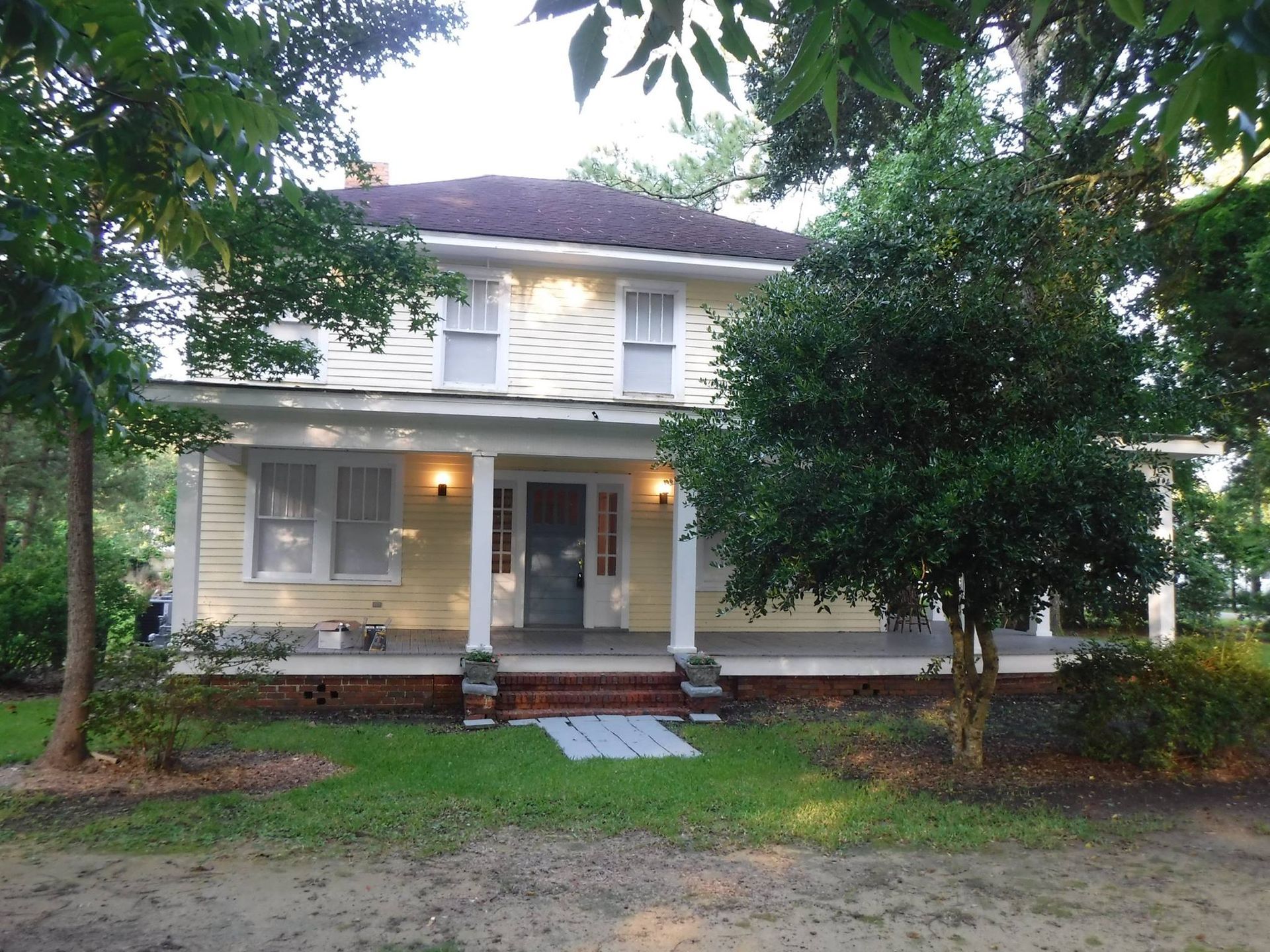 Yellow two-story house with porch, trees, and walkway leading to the front door.