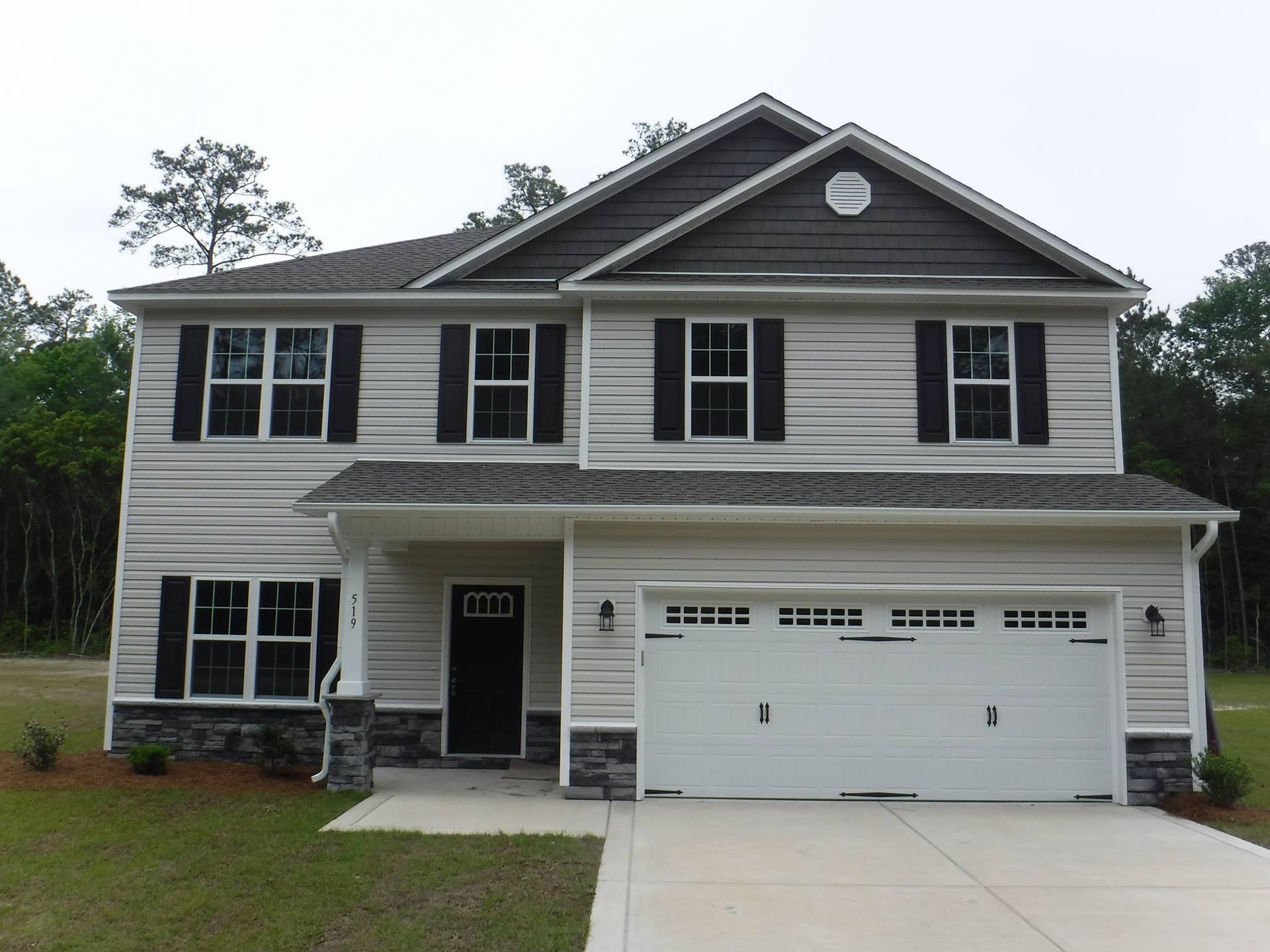 Two-story house with light siding, dark shutters, black door, and a two-car garage.