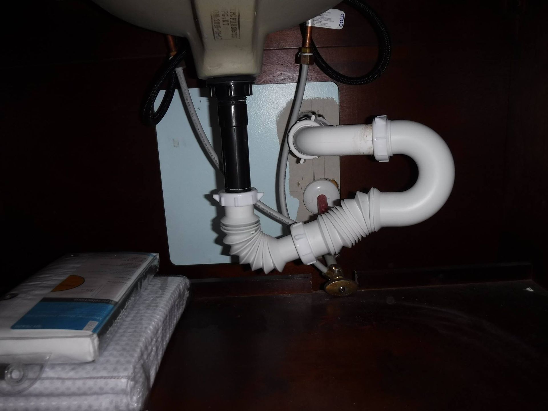 White bathroom sink drain pipes under a brown cabinet, showing a flexible drain.