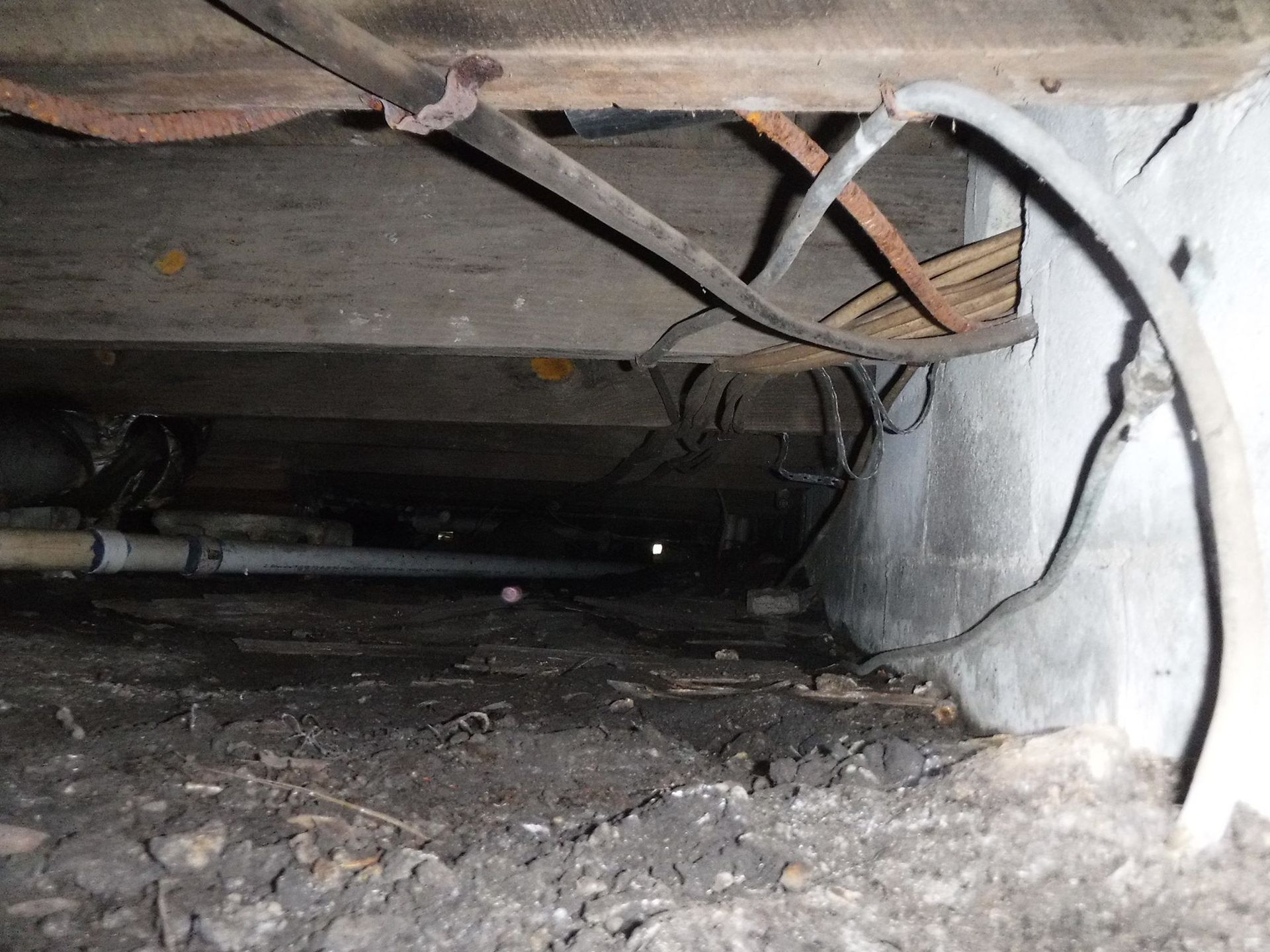 Dark crawl space with pipes, electrical wires, and concrete wall.