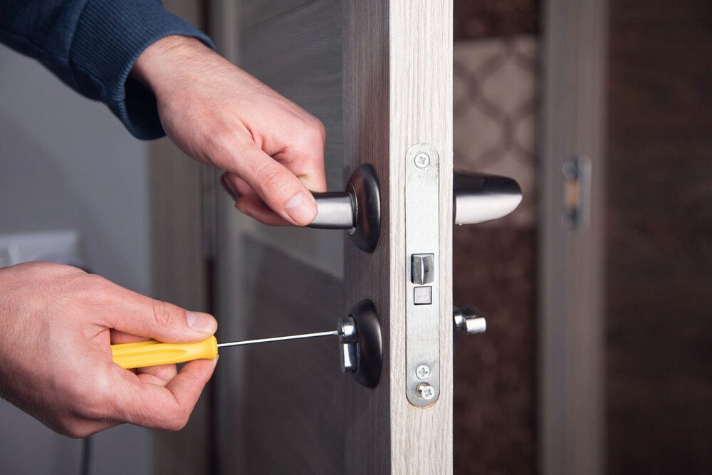 Person Using a Screwdriver to Fix a Door Handle on a Light-colored Door — Coast 2 Coast Locksmiths in Pelican Waters, QLD