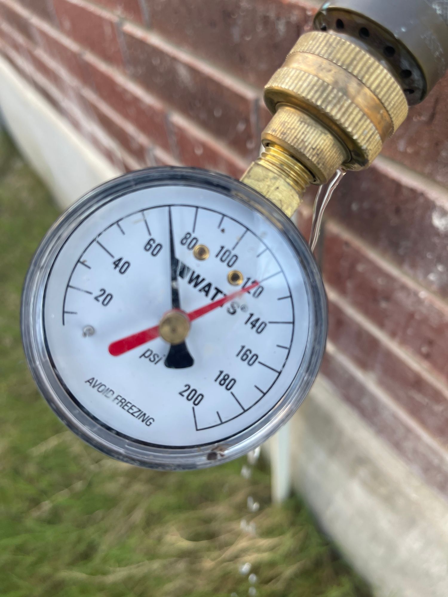 A pressure gauge is attached to a hose on a brick wall.