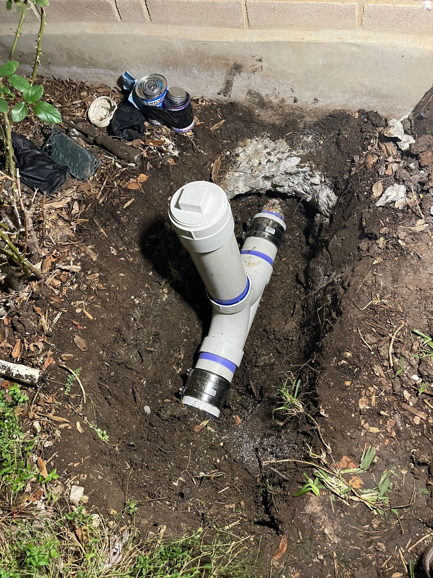 A drain pipe is sitting in the dirt next to a brick wall.