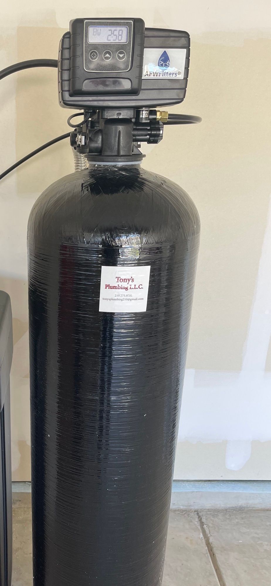 A black water softener is sitting on a tiled floor next to a wall.