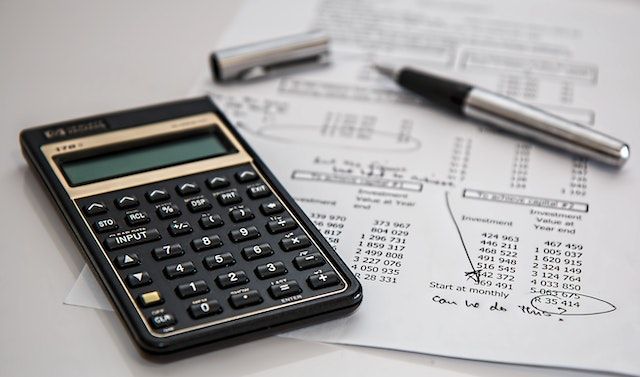 Black financial calculator next to an open silver pen and on top of a printed document with numbers on it