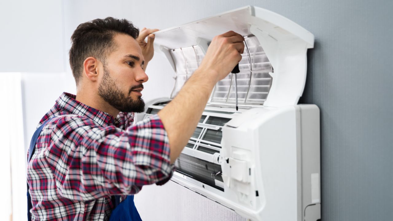 Person in a flannel shirt using a screwdriver to work on an air conditioning unit