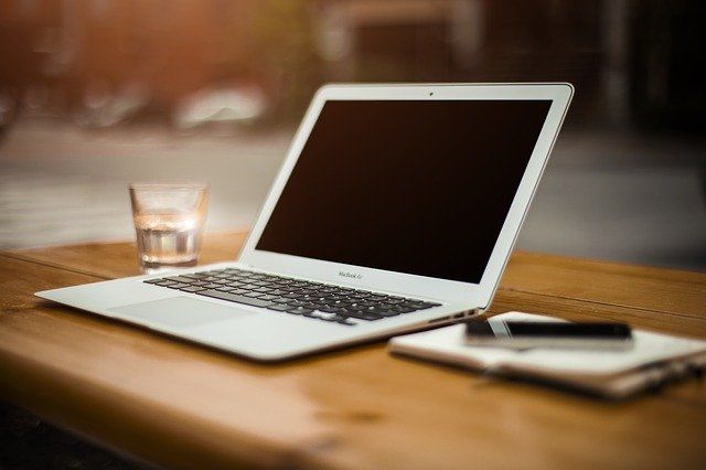 A desk set up with a notebook, laptop, and glass of water