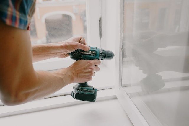 Pair of hands holding a power drill near a white window