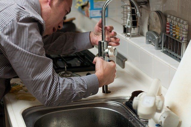 Person fixing a faucet on a kitchen sink