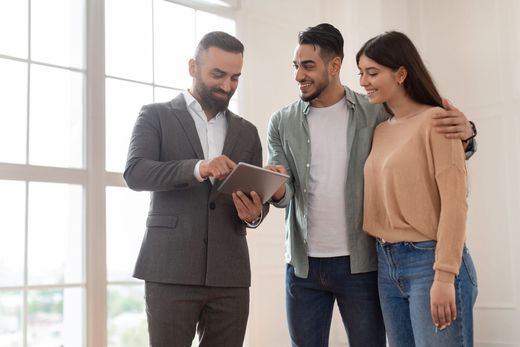 A person in a suit shows a tablet to a couple in a sunlit room.