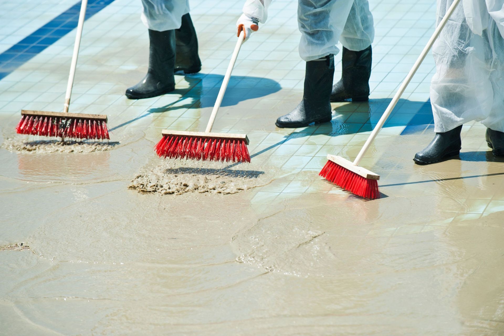 Workers sweeping wet concrete with red brooms on a construction site