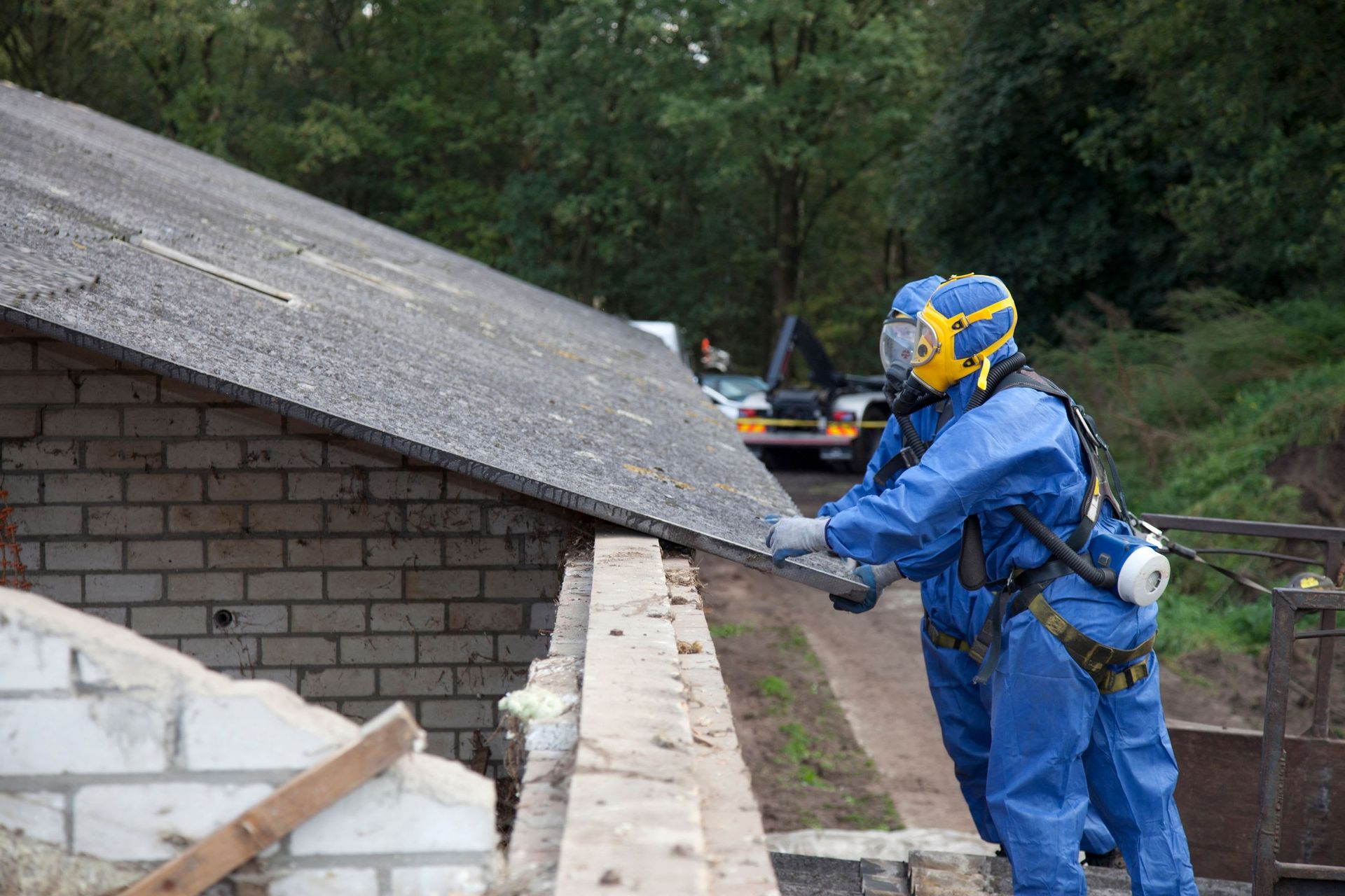 Worker in blue safety gear inspecting a damaged roof on a brick building.