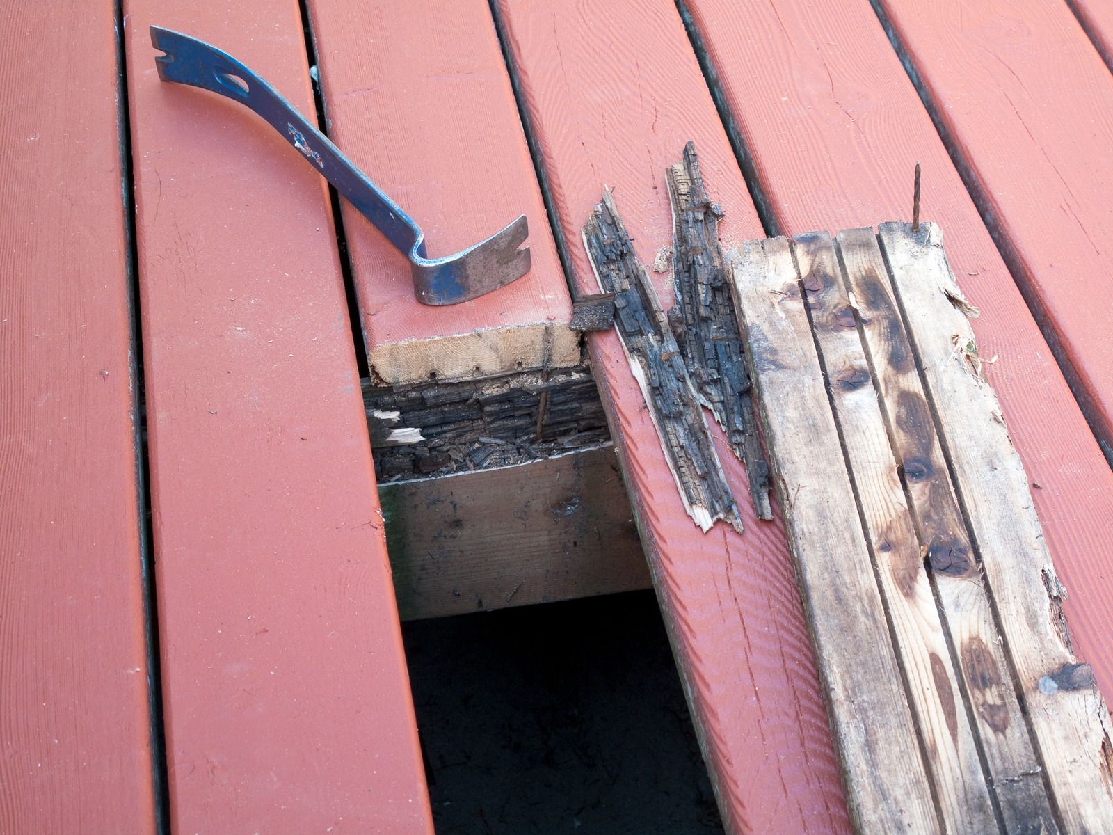 A hammer is sitting on a wooden deck next to a piece of wood.