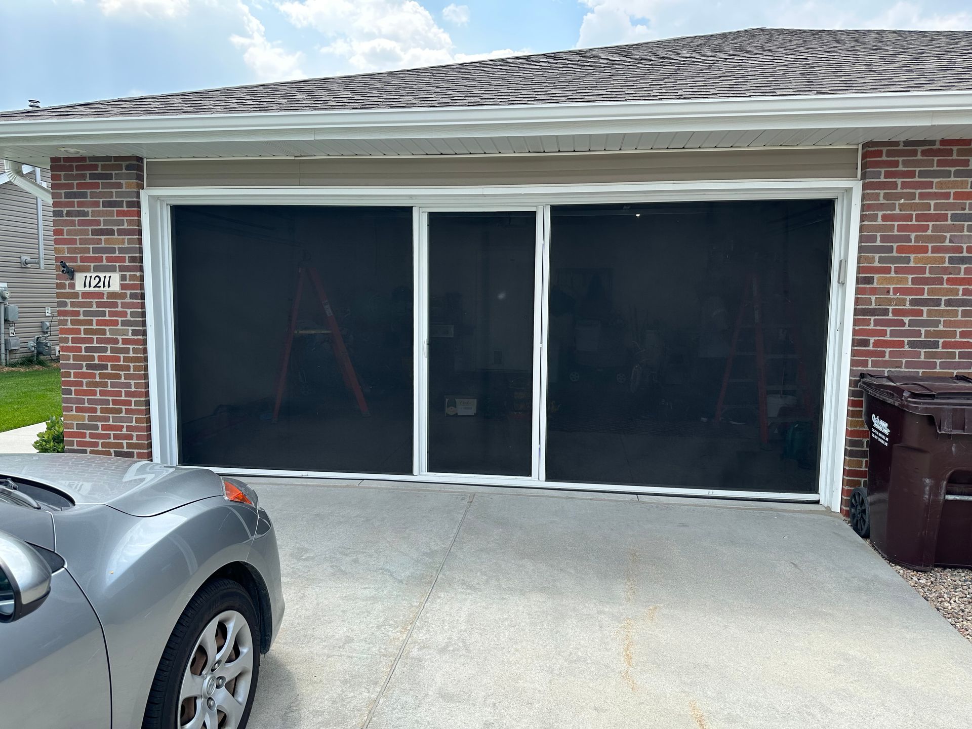 A car is parked in front of a screened in garage door.