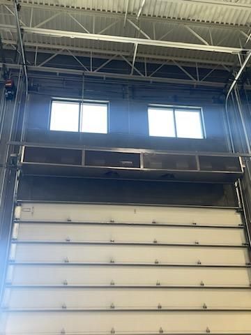 A large garage door is open in a building with two windows.