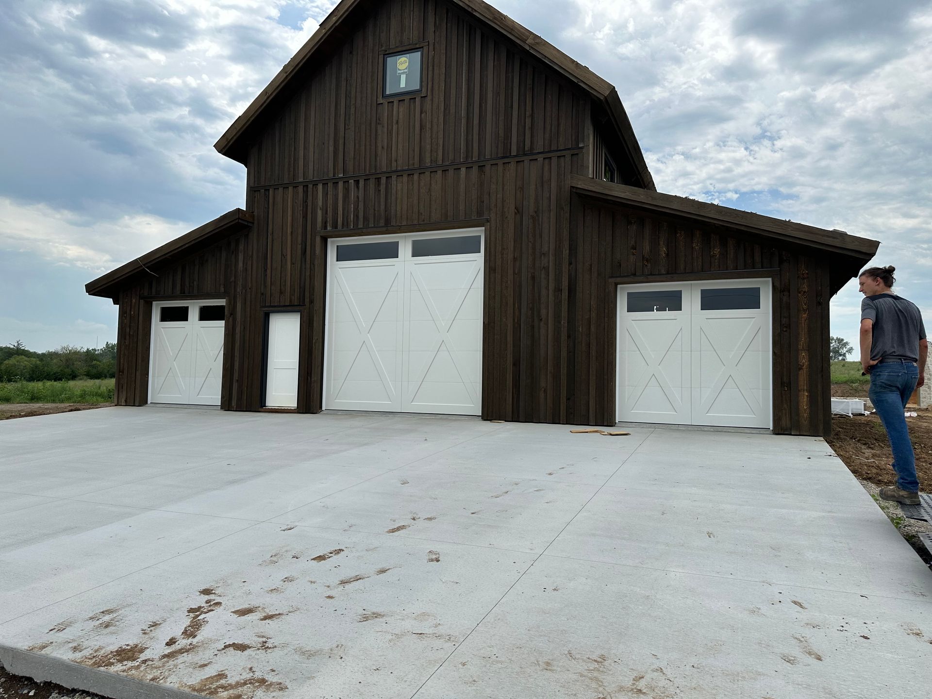 A man is standing in front of a barn with three garage doors
