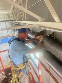 A man is standing on a ladder working on a pipe.
