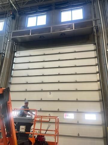 A man is standing on a lift in front of a large garage door.