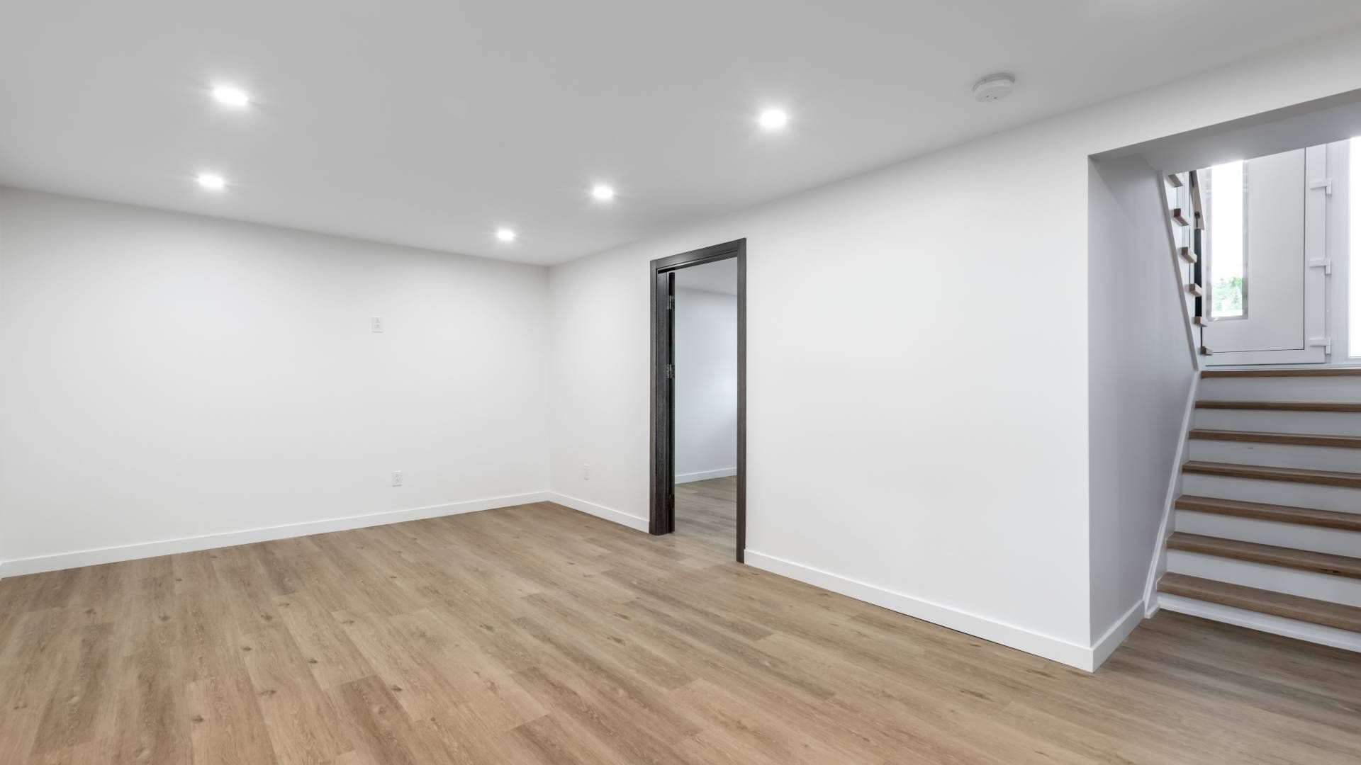 An empty basement with hardwood floors and white walls.