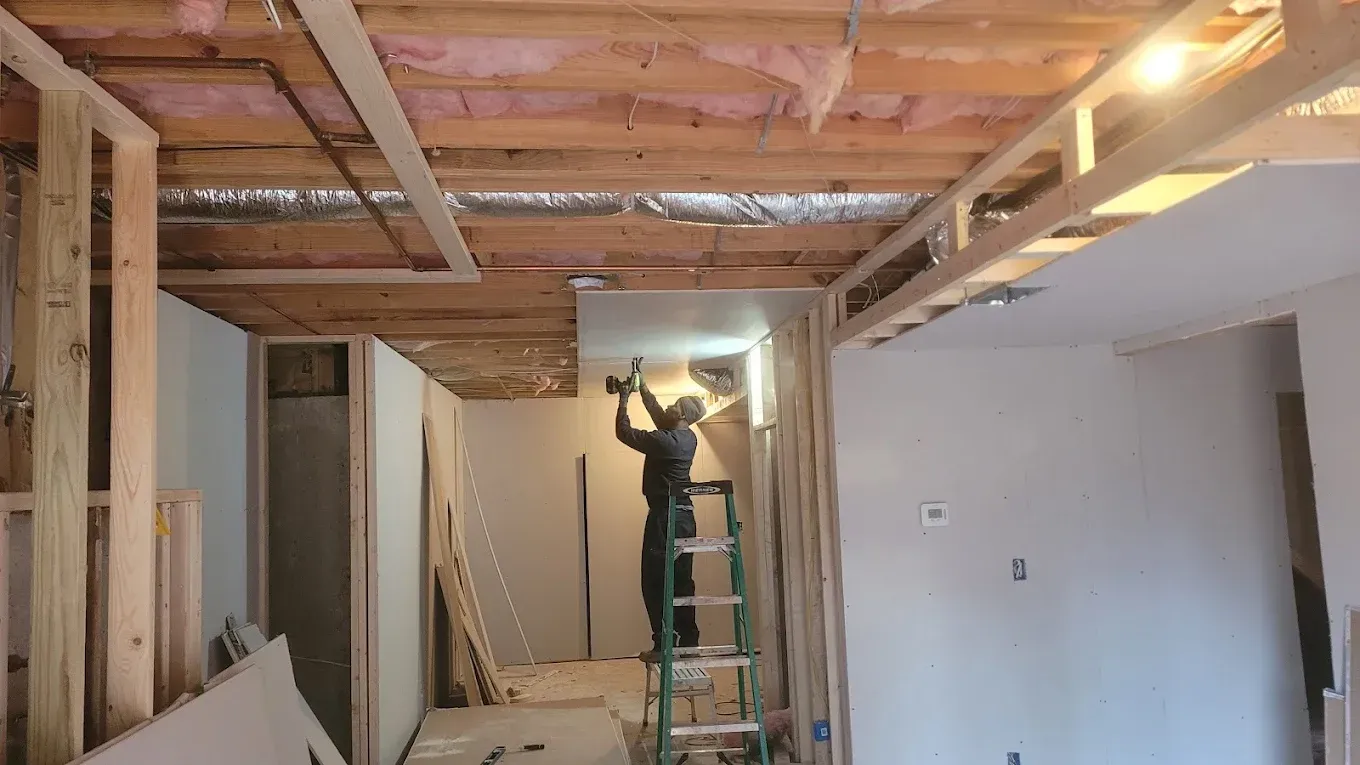 A man is standing on a ladder in a room under construction.