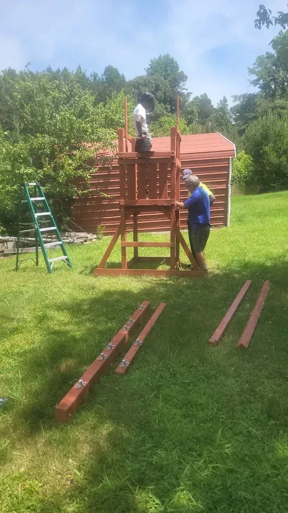 Two men are working on a wooden playground in a backyard.